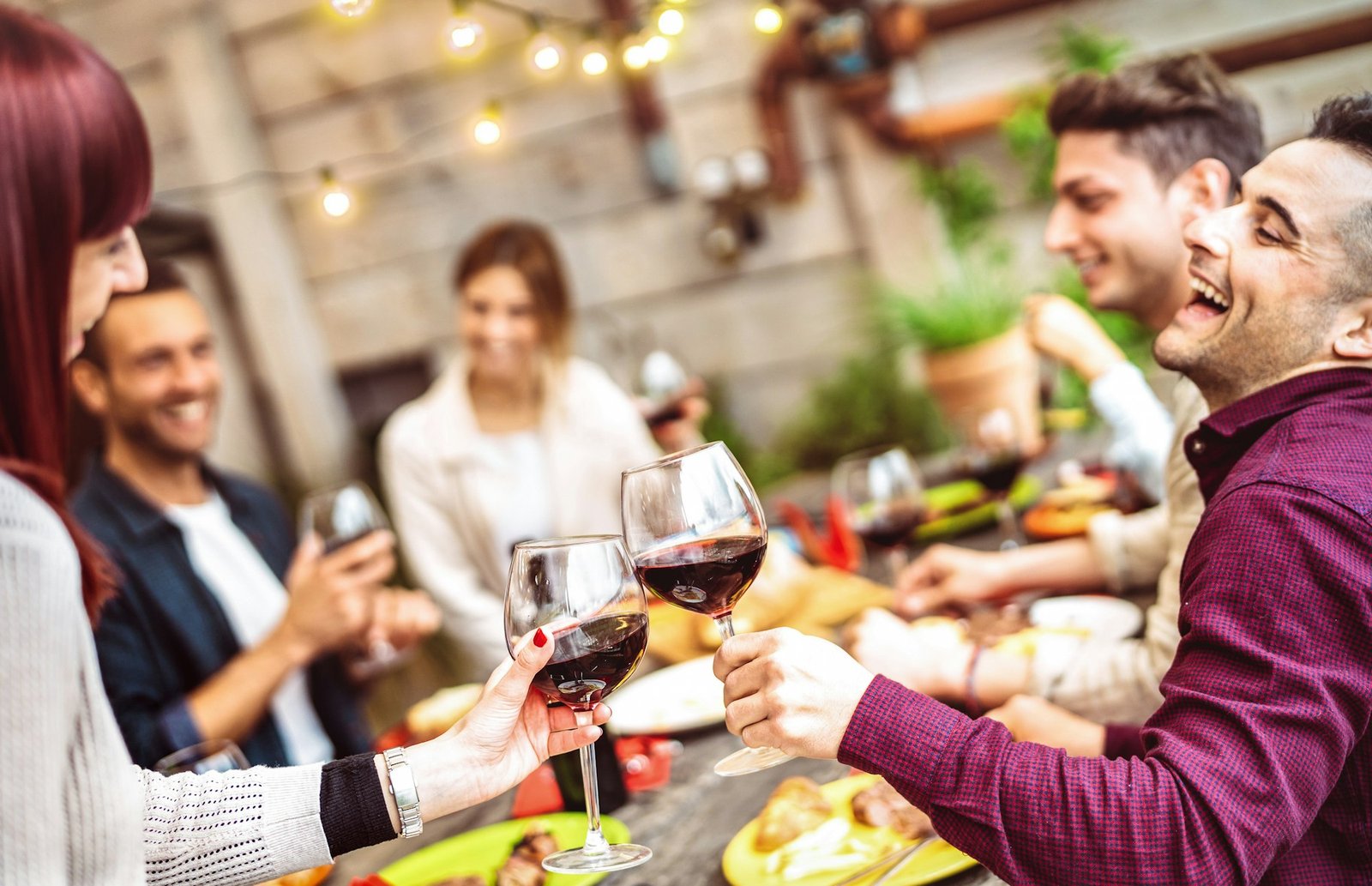 Happy friends having fun drinking red wine on balcony at private dinner party