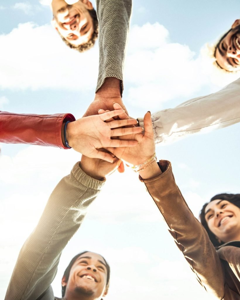 Multiracial happy young people stacking hands outside