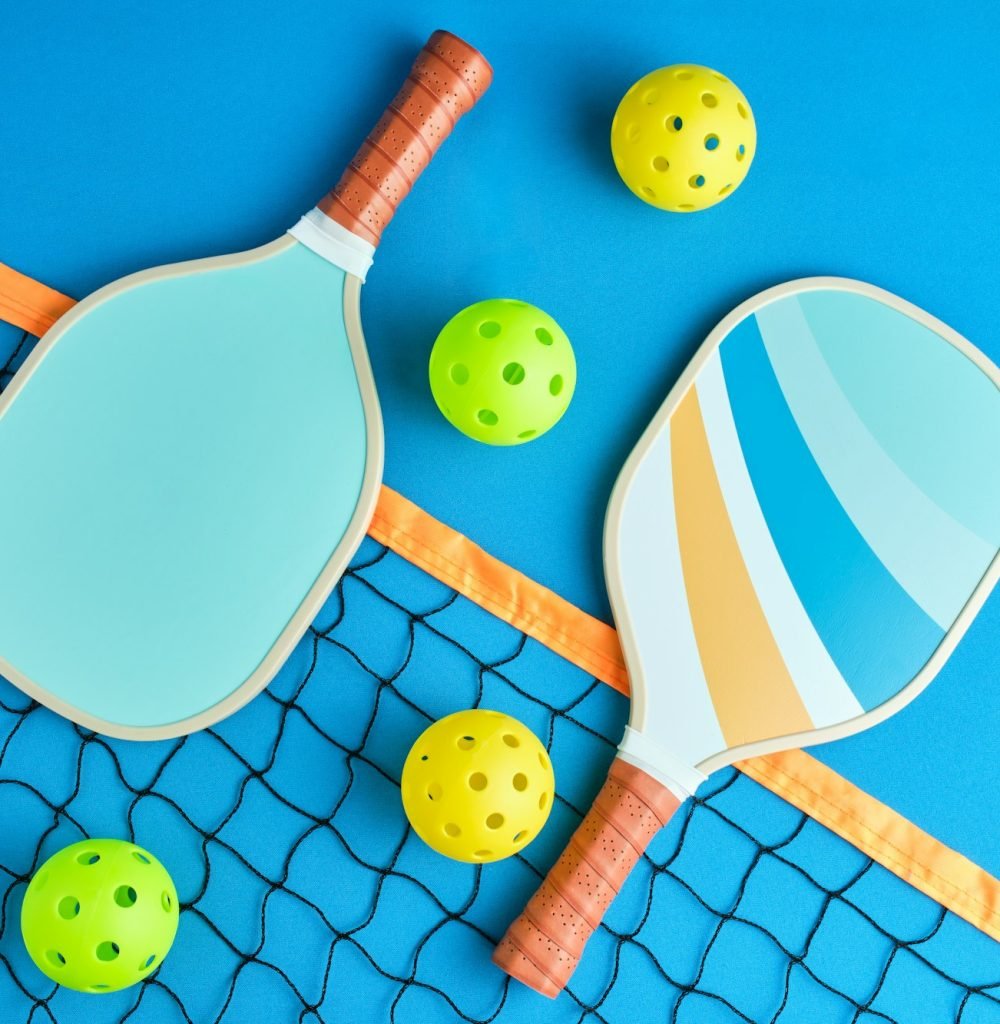 two paddles and four pickleball balls on top of a net on blue background