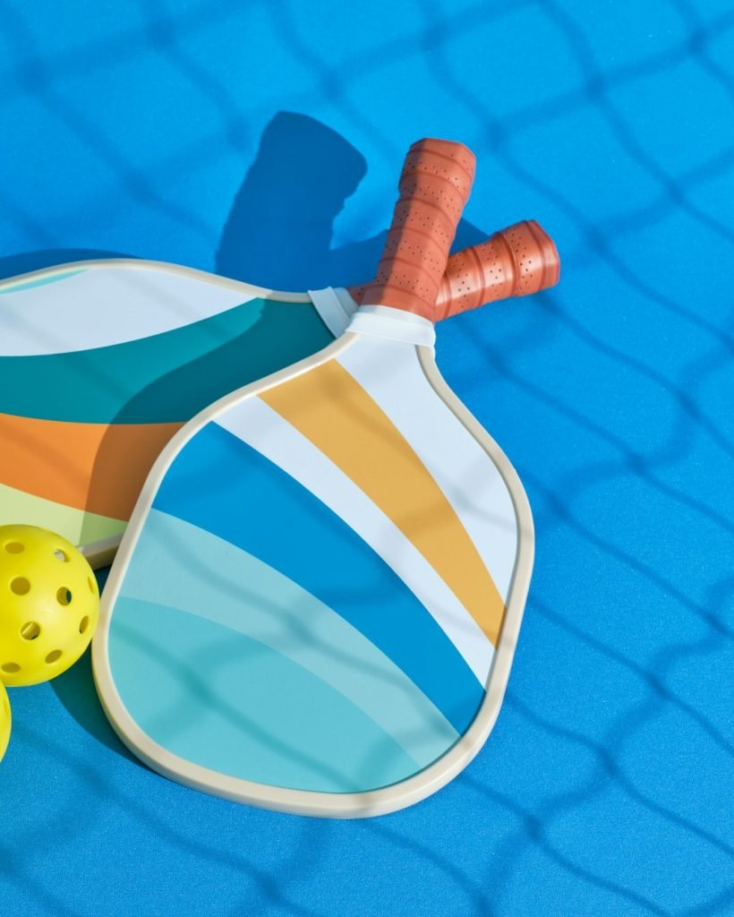 two pickleball paddles with some balls next to them with the shadow of a net in front